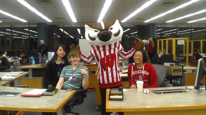 three girls sitting at desks with an image of a creature in the background