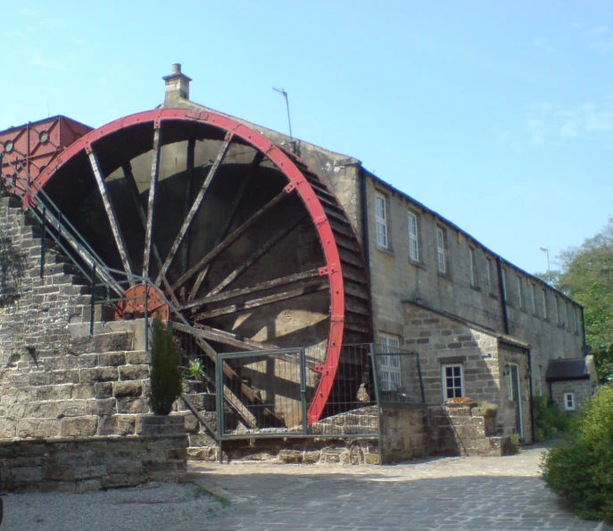 an old water wheel by the road near a building