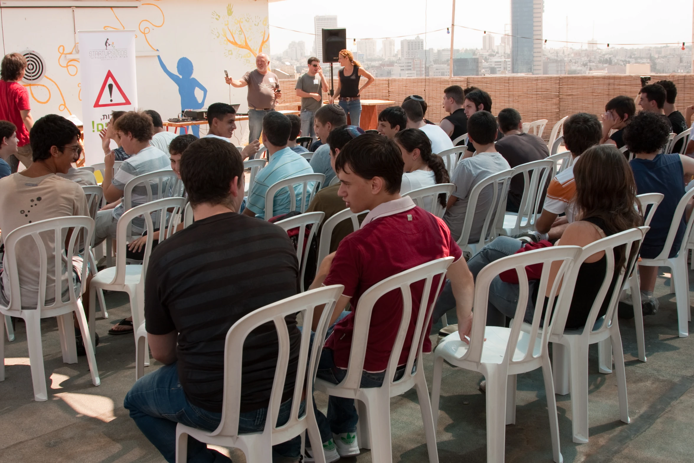 a man speaking to a group of people in white chairs