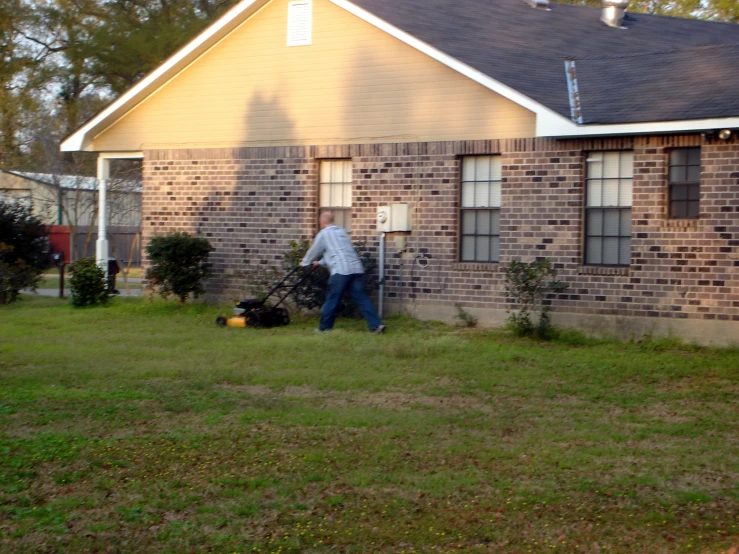 man with his mower in the grass next to brick house