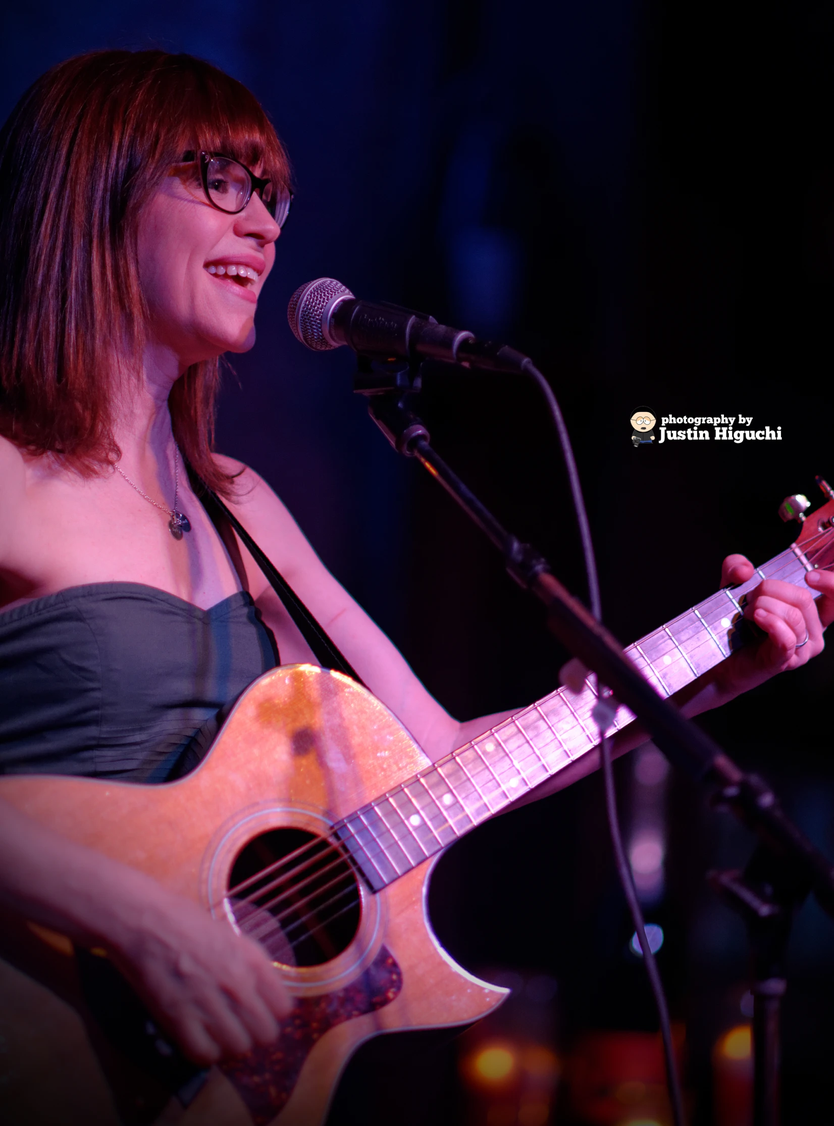 a woman in glasses holds a guitar and sings