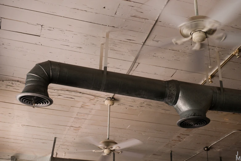 a ceiling fan and two large duct wrapped pipes hanging from the ceiling