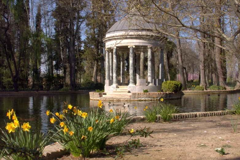 gazebo near water with yellow flowers in the foreground