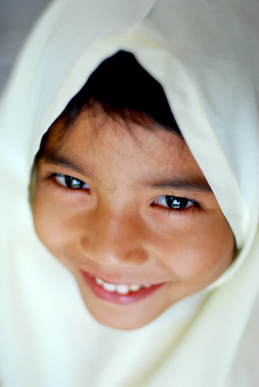 a child smiling under a white sheet in a studio