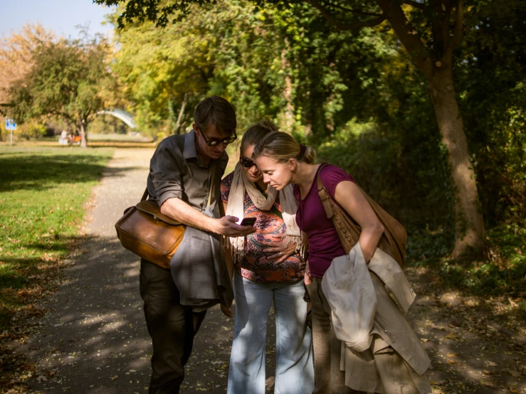 two people on a road using a cellphone and another woman is looking at the ground