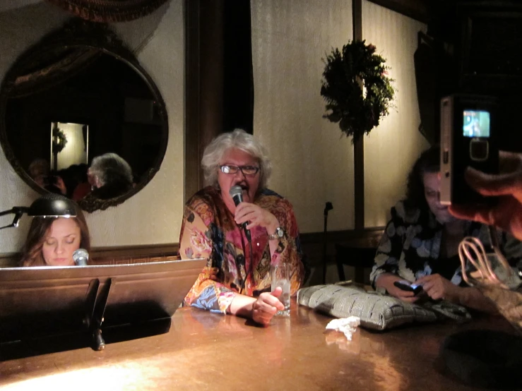 an elderly woman is singing into the microphone while three other women are waiting