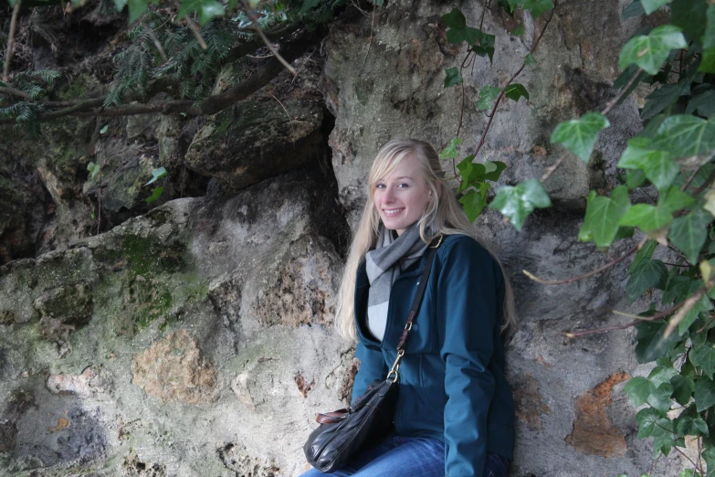 a young blonde woman in a blue jacket is sitting on the ground