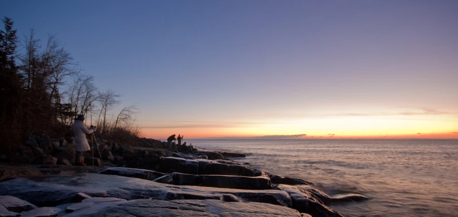 people standing on rocks watching the sunset