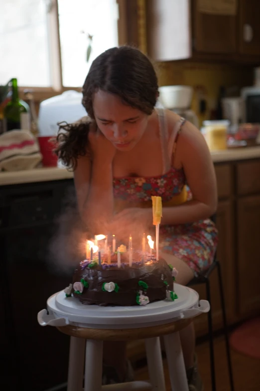 woman in a kitchen blowing out candles on a cake