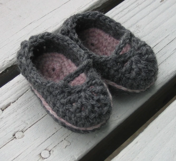 a pair of gray crocheted slippers are resting on a wooden bench