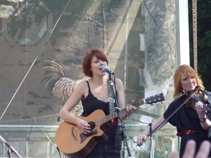 two women standing on stage, one playing guitar