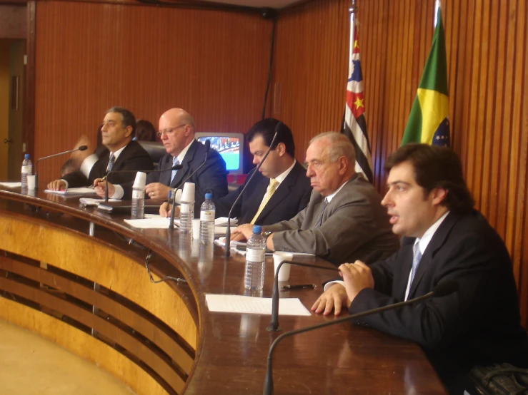 several people sitting in front of microphones at a long conference table