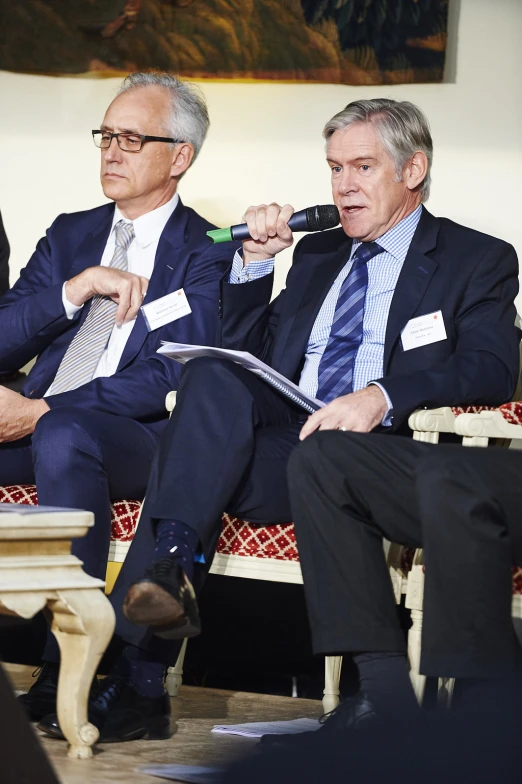 two men are sitting on the coach in suits