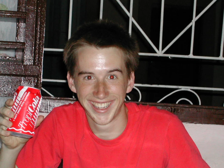 a young man smiles while holding a can of soda