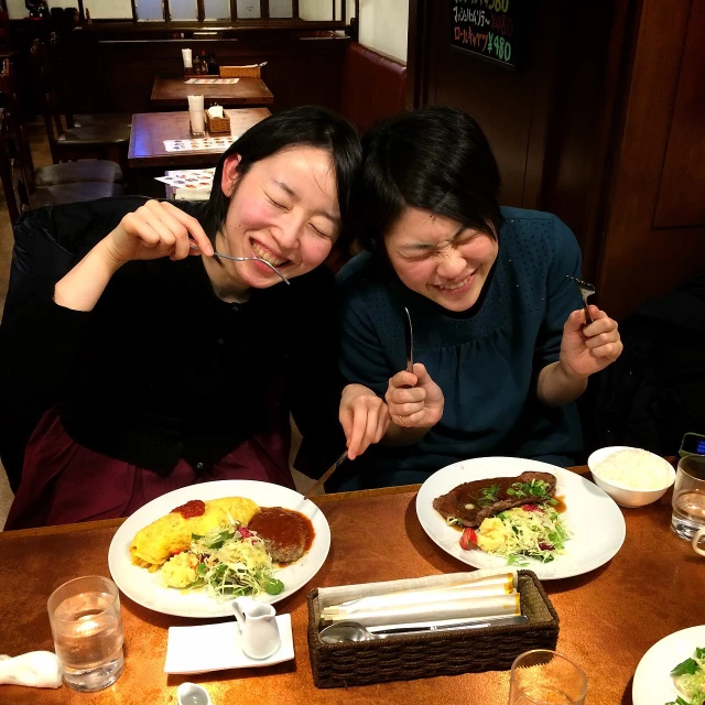 two women are posing for the camera at a table with their plates