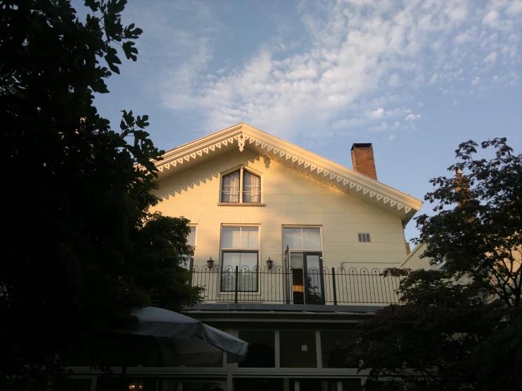 a two story white house with the evening sun peeking over it