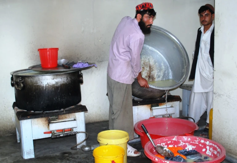 two men stand around pots and pans with a large pot on top