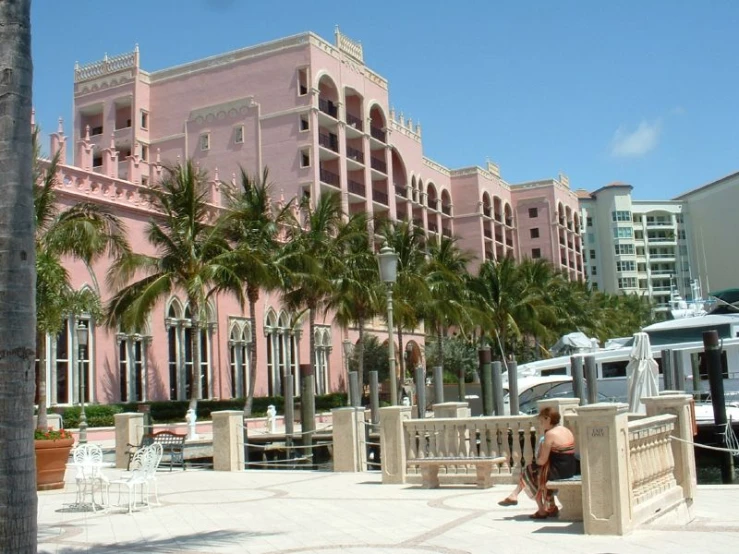 woman sitting at end of pier between palm trees and buildings