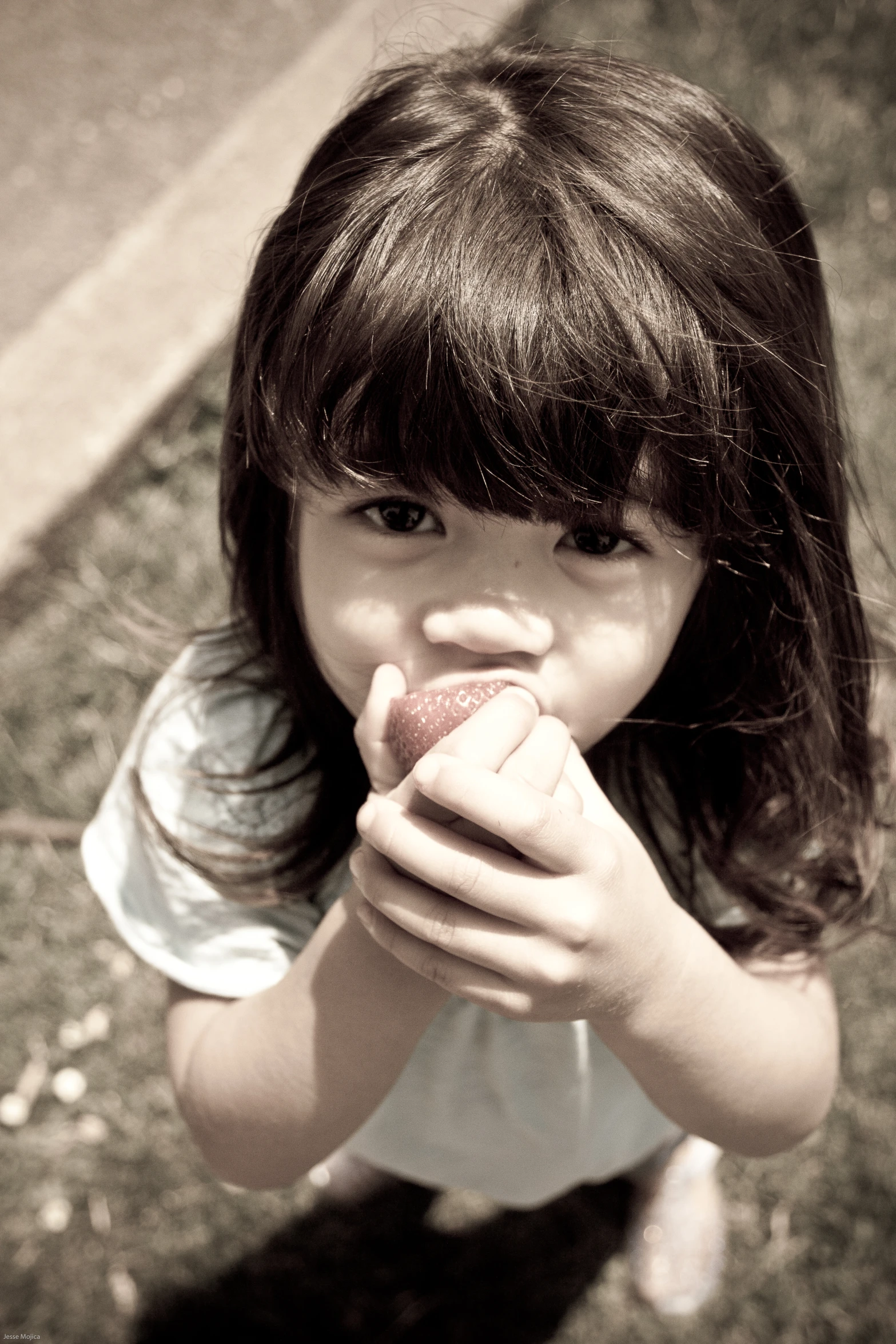 a young child eating an apple outside on the ground