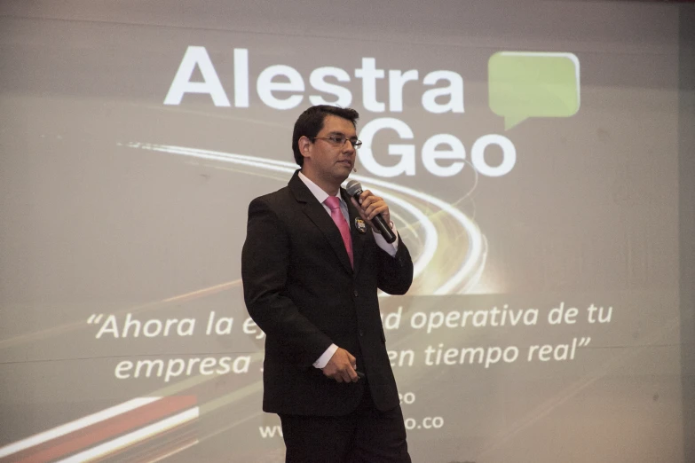 a man stands in front of a large projection screen, in front of a microphone