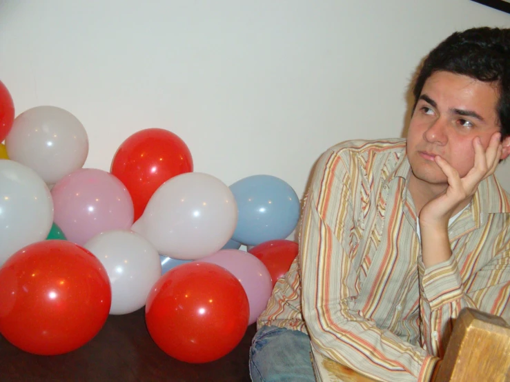 a man sitting at a table next to balloons and a clock