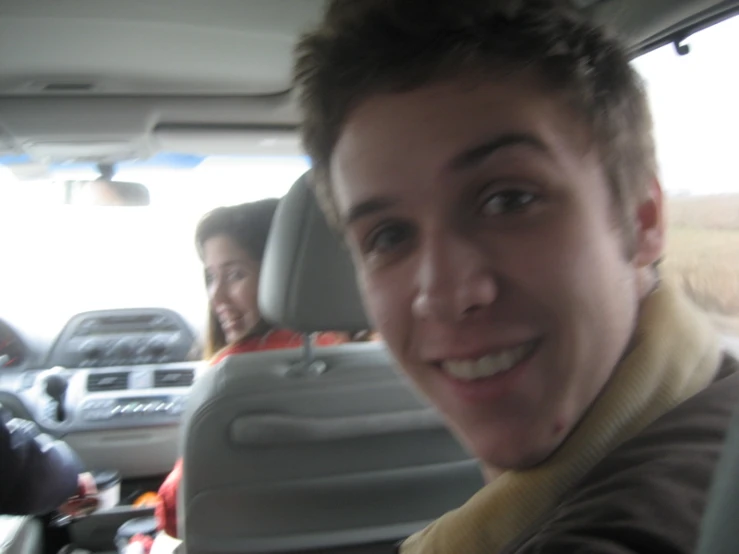 a smiling man riding in a car down a street