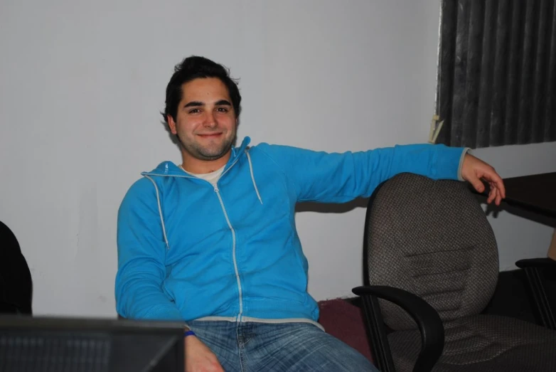 a man with a blue hoodie sitting next to a chair