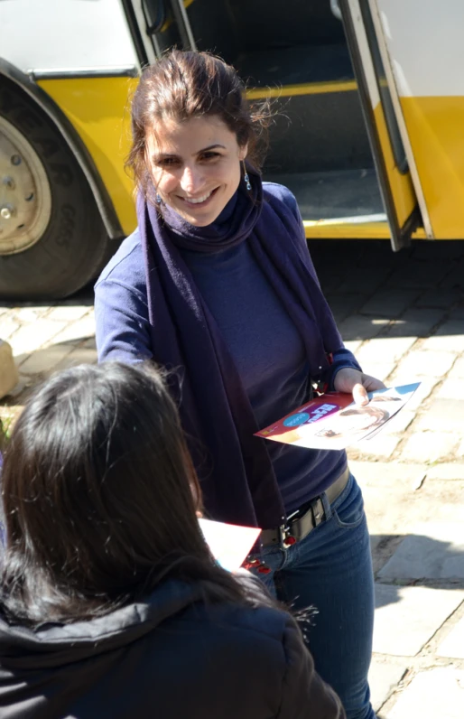 a woman is holding a sheet with pictures of people next to a bus