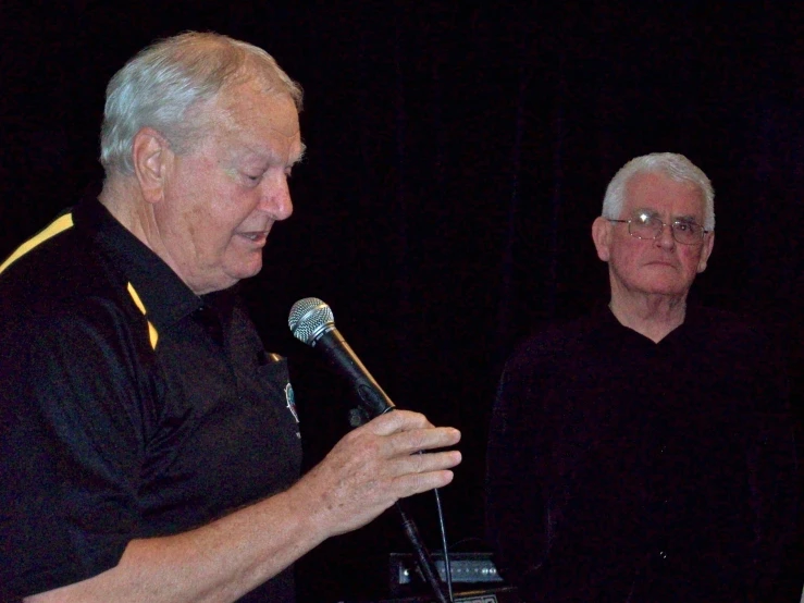 a man in black holding a microphone next to another man