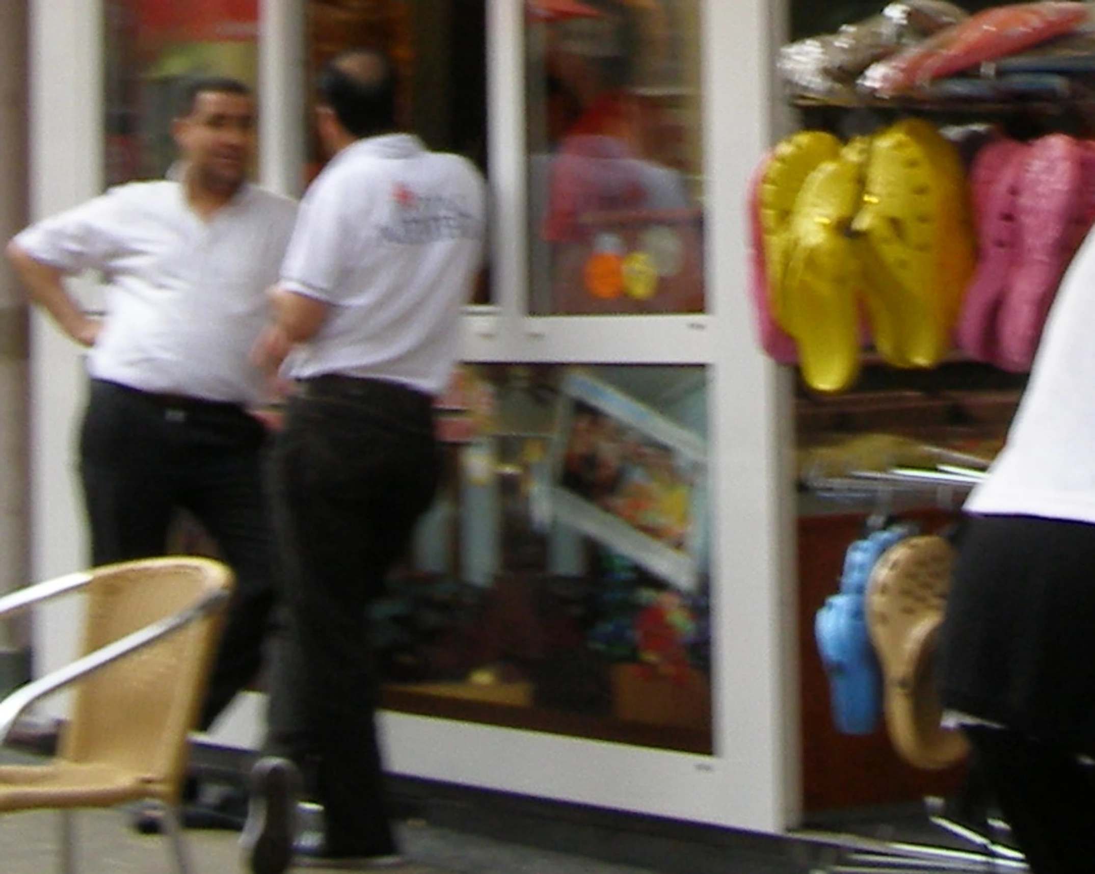 a man stands in front of a shoe store while another person walks past it