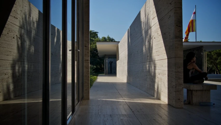 a woman sits on a bench and looks out the window of an empty hallway