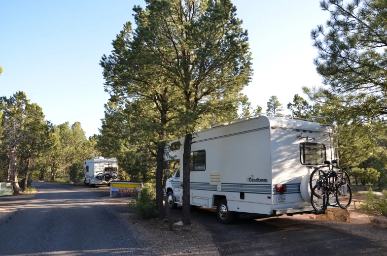 an rv sits parked by the side of the road with bicycles leaning against a tree