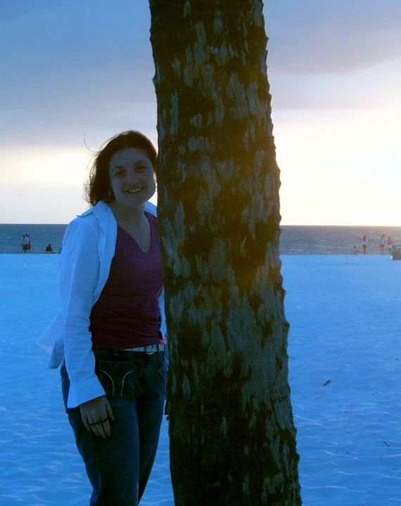 a woman leans against the base of a palm tree