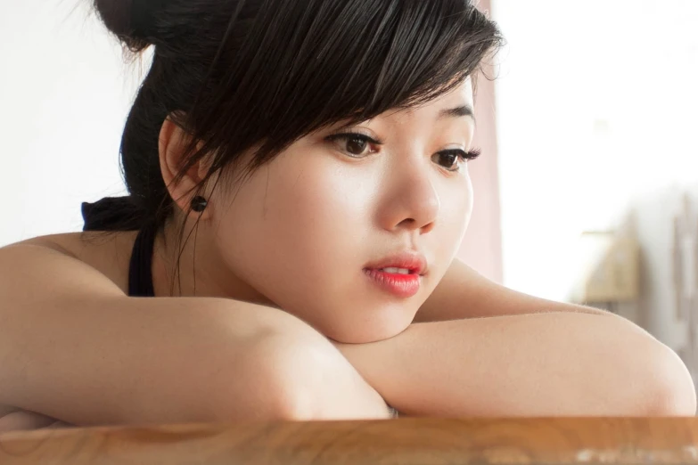 a asian girl leaning on top of a wooden desk