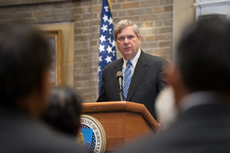 a man in suit and tie at a podium talking to people