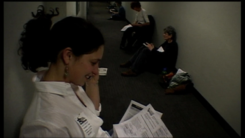 the woman is looking at the paper as another sits on the floor behind her