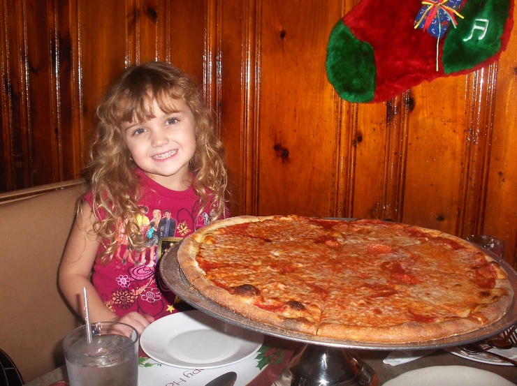 little girl sitting in front of a large pizza pie