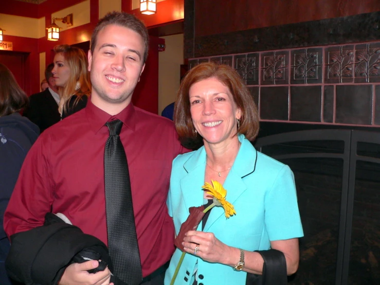 a man wearing a tie is standing next to a woman with a flower in her lap