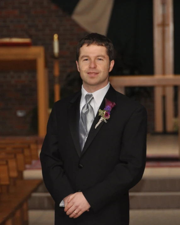 a man in a black tuxedo is standing by the alter