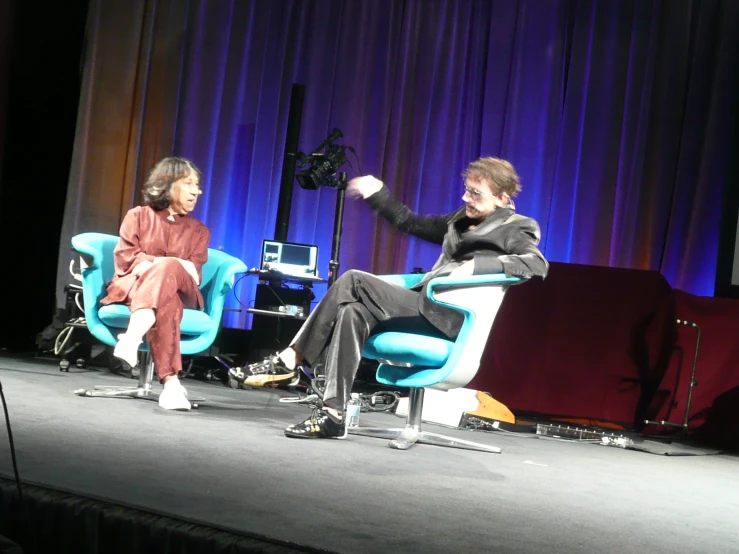 two people sitting on chairs on stage speaking