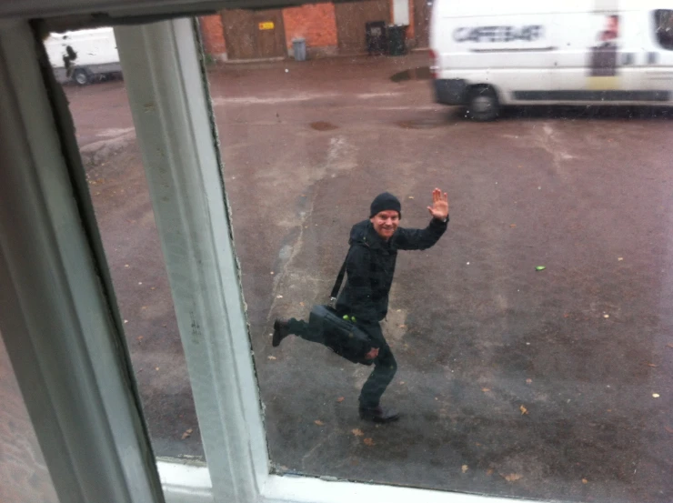 man in black jacket standing outside window with one hand up