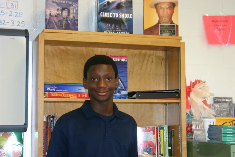 a boy smiling while standing next to a book shelf