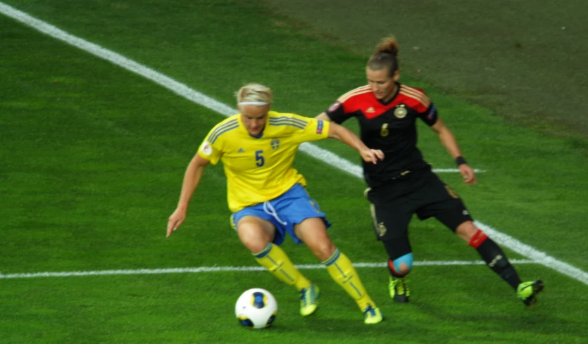 two women in soccer uniforms running after a soccer ball