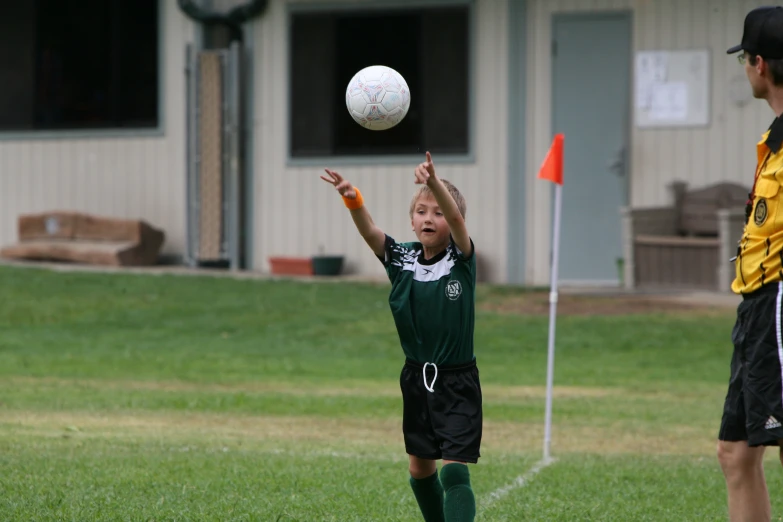 a  in green shorts and a yellow shirt trying to catch a white soccer ball