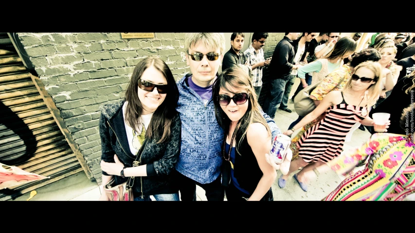 three people stand together in front of a brick wall