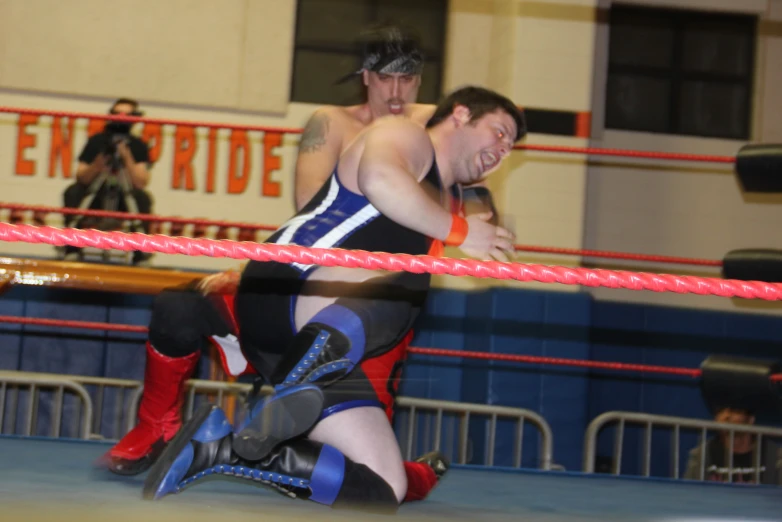 two men wrestling during a competition with red ropes