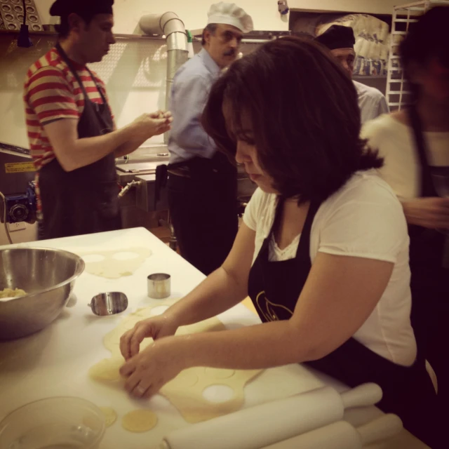 a woman rolling up dough at a table with other people around her