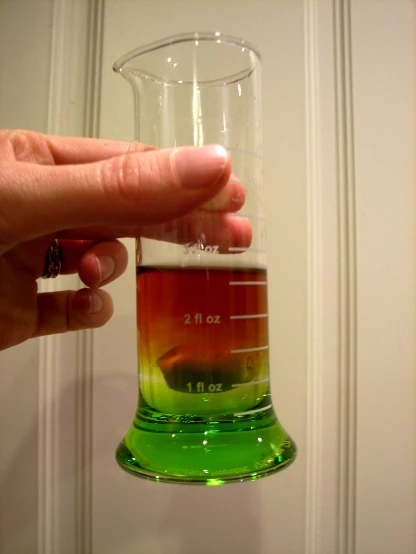 the person holding the beaker has an orange yellow green liquid in it