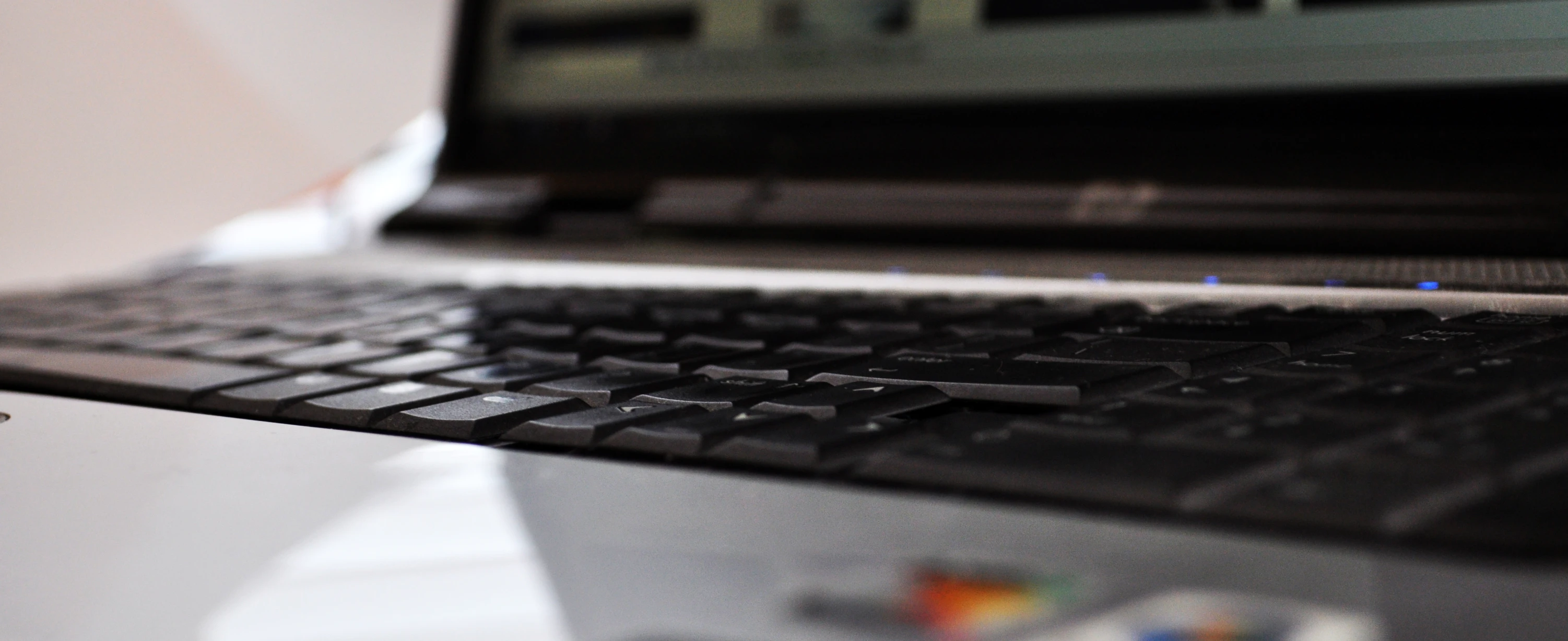 the keyboard of an open laptop with other objects in the background