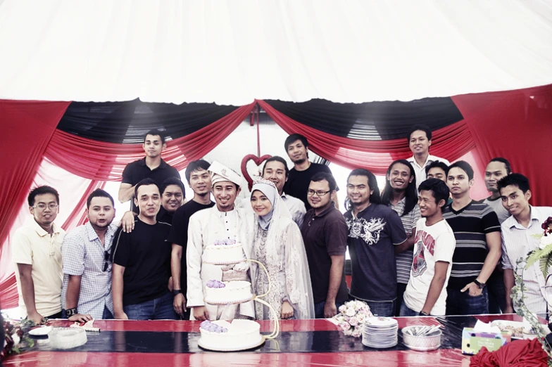 group of people standing in front of the cake at a wedding